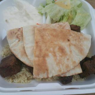 A takeout meal featuring pita bread, meat, rice, salad, and tzatziki sauce.