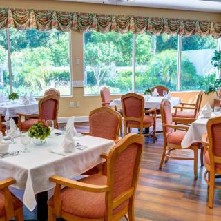 A well-lit dining area with neatly arranged tables and chairs, offering a view of the lush greenery outside through large windows.
