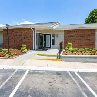 A small brick building with a parking lot and landscaped entrance on a sunny day.