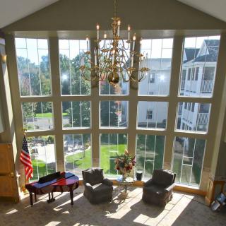A spacious room with large windows, a chandelier, and a seating area, featuring an American flag and a piano.