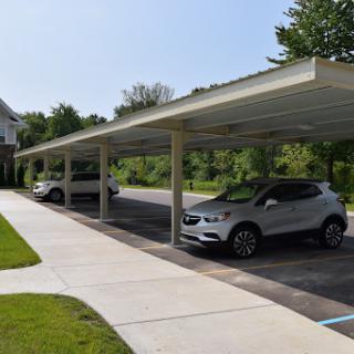 A view of a carport with two parked cars, surrounded by greenery and clear blue skies.