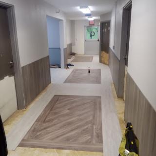 A view of a well-lit apartment hallway with patterned carpets and doors on either side.
