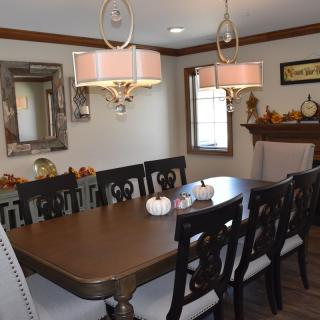 A well-decorated dining room featuring a large table with chairs and elegant chandeliers, complemented by a mirror and seasonal decorations.