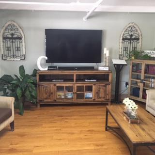 A cozy living room featuring a modern TV setup, wooden furniture, and decorative plants.