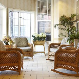 A cozy living room with wicker furniture and indoor plants illuminated by natural sunlight.