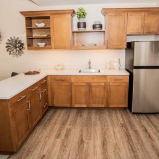 A modern kitchen with wooden cabinets, a stainless steel refrigerator, and wood flooring.