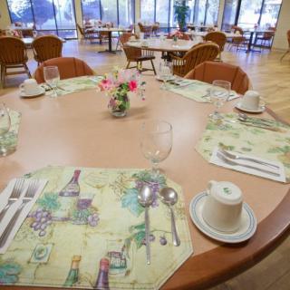 A neatly arranged dining table in a restaurant setting, complete with cups, cutlery, and floral centerpiece.