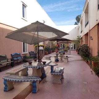 A courtyard with tables and chairs, shaded by umbrellas, surrounded by plants and buildings.