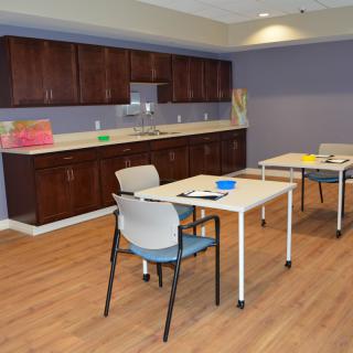 A tidy room with tables, chairs, and a kitchen area featuring wooden cabinets.