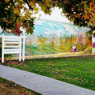 A scenic mural depicting a landscape is framed by autumn trees and a sidewalk.