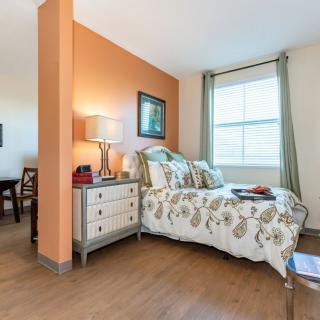 A cozy bedroom with a floral bedspread, side table with a lamp, and a large window.