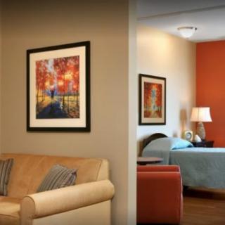 A cozy living space with a view into an adjoining bedroom, featuring elegant artwork and warm lighting.