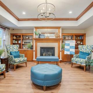 A cozy living room featuring a central fireplace, surrounded by patterned armchairs and a blue ottoman, with built-in wooden shelves adding charm to the space.