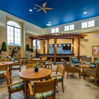 A spacious lounge area with tables and chairs, featuring a high blue ceiling and large windows.