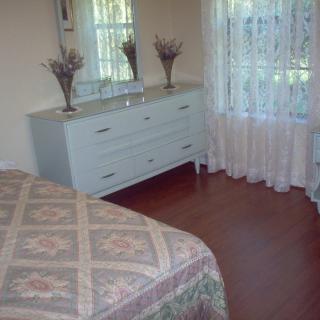 A cozy bedroom with a dresser and mirror, featuring floral decorations and sheer curtains.