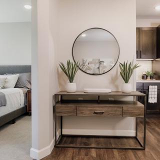 A modern and minimalist interior features a console table with plants, a round mirror, and wood flooring in a bedroom setting.