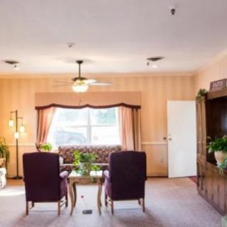 A cozy living room with armchairs and a window, decorated with plants and a ceiling fan.