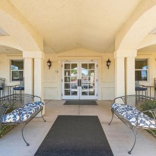 The covered entrance of a building with benches on either side and glass double doors.