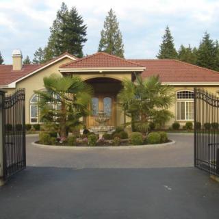 A gated residential house with a circular driveway and landscaped front yard.