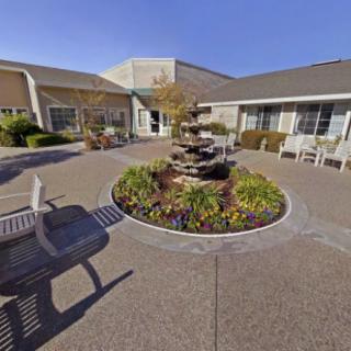 A serene courtyard featuring a central fountain, surrounded by landscaping and benches, with building exteriors in the background.