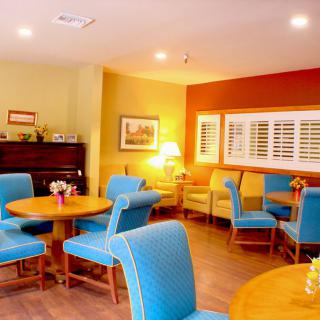 A cozy dining area with blue chairs, wooden tables, and a piano in the corner.