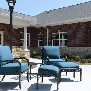 A set of blue cushioned outdoor chairs arranged on a sunny patio, surrounded by well-maintained landscaping.