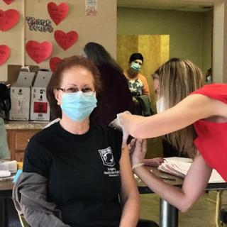 A woman receiving a vaccine while wearing a mask in a community healthcare setting.