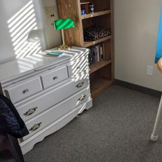 A cozy corner of a room featuring a white dresser, a green lamp, and a bookshelf.