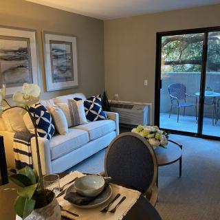A cozy living room with a sofa, coffee table, and a dining area, leading to a balcony with outdoor seating.