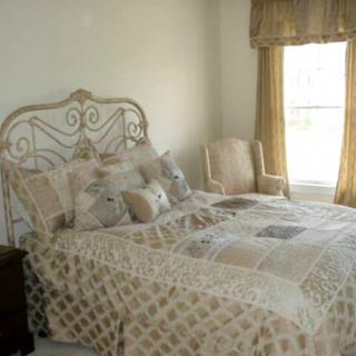 A cozy bedroom with a quilted bedspread, decorative pillows, and an upholstered chair by the window.