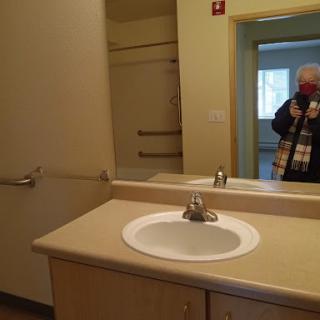 A view of a simple bathroom featuring a sink, mirror, and handrails.