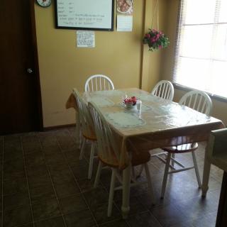 A cozy dining area with a table set for four, featuring a flower vase centerpiece and natural light streaming in from the window.