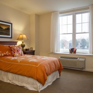 Cozy bedroom with orange bedding and a large window.