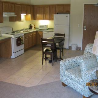 A cozy apartment kitchen with wooden cabinets, a small dining table, and an armchair.