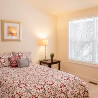 A cozy bedroom with a floral-patterned bedspread, a bedside table with a lamp, and a large window letting in natural light.