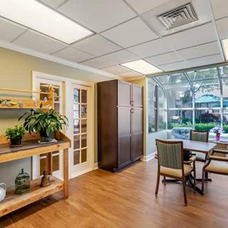 A bright and welcoming office meeting area featuring a table with chairs, large windows, plants, and wooden flooring.