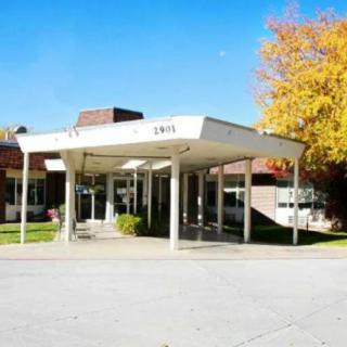 A building entrance with a canopy, surrounded by autumn trees.