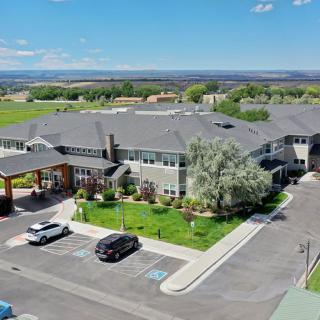 Aerial view of a large building with a parking lot, surrounded by greenery and fields under a clear blue sky.