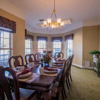 A spacious dining room with an elegant table set for a meal, featuring a central chandelier and large bay windows providing ample natural light.