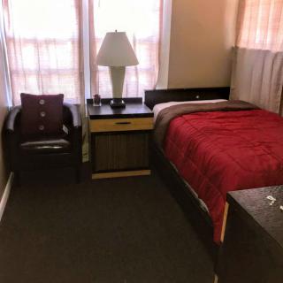 A cozy bedroom setup with a single bed, nightstand, lamp, and chair.