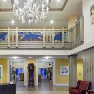 A well-lit lobby featuring a chandelier, balcony, and a grandfather clock.