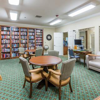 A cozy library interior with bookshelves, a round table, chairs, and a computer workspace.