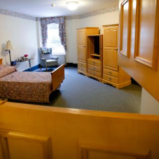 A spacious hotel room featuring a bed, a television stand, and a window with natural light.