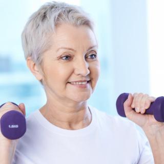 An elderly woman exercising with dumbbells indoors.