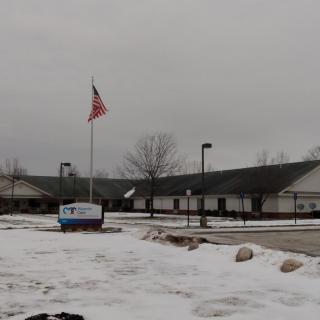 A building with an American flag in a snowy parking lot on a cloudy day.