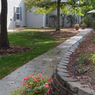 A landscaped garden pathway bordered by flowers and trees leading to a house.