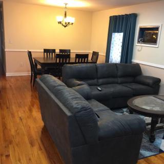 A cozy living room with a connected dining area, featuring comfortable sofas and a wooden dining set.