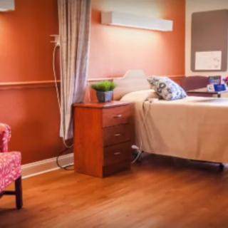 A cozy bedroom with warm-toned walls, featuring a bed, nightstand, and an armchair.
