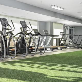 A modern gym with treadmills and elliptical machines lined up beside a turf-covered floor.