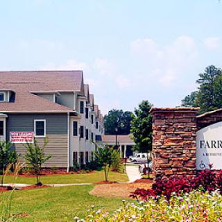 A view of an apartment complex featuring well-maintained landscaping and a welcoming sign.